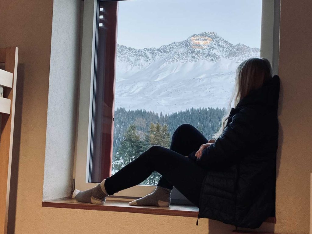 Eine Frau sitzt im Fenster und schaut aufs Bergpanorama.