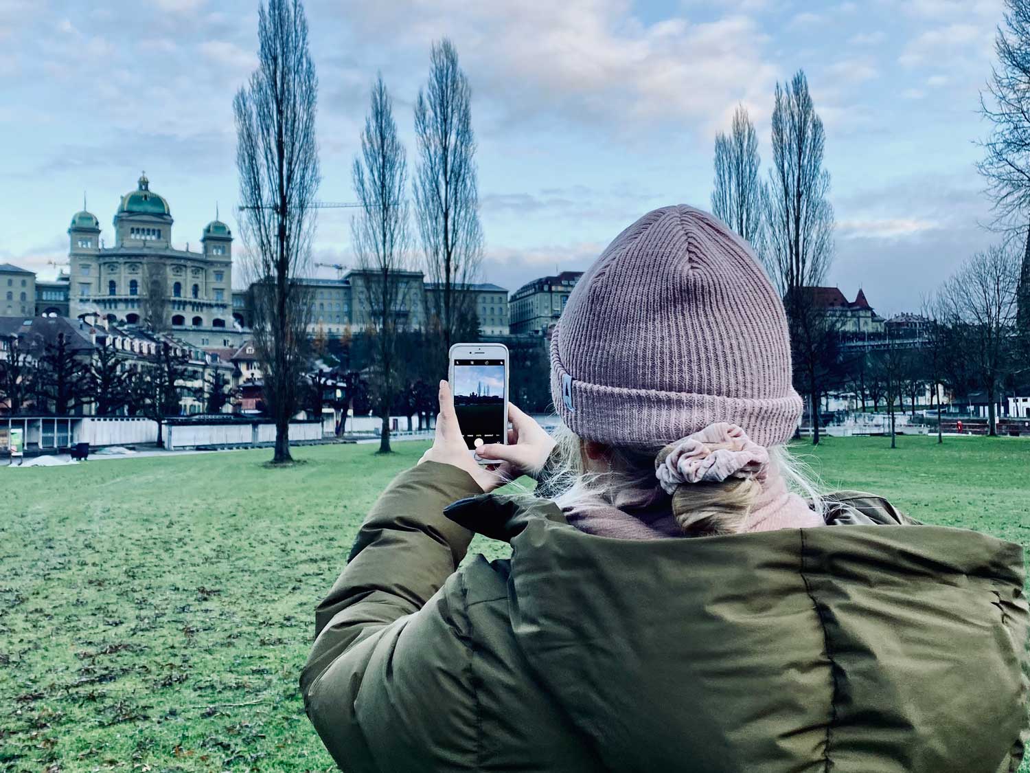 Eine Frau die mit dem Handy ein Bild vom Bundeshaus Bern macht.